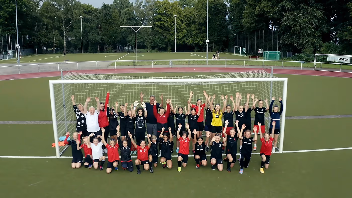 Imagefilm Szene: Fußballmannschaft mit Trainerinnen und Trainern jubelt vor dem Tor auf dem Sportplatz – inspirierende Darstellung von Teamgeist, Bildung und Zusammenhalt im Imagefilm Stadt Dortmund.