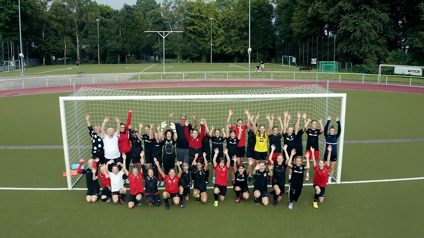 Imagefilm Szene: Fußballmannschaft mit Trainerinnen und Trainern jubelt vor dem Tor auf dem Sportplatz – inspirierende Darstellung von Teamgeist, Bildung und Zusammenhalt im Imagefilm Stadt Dortmund.