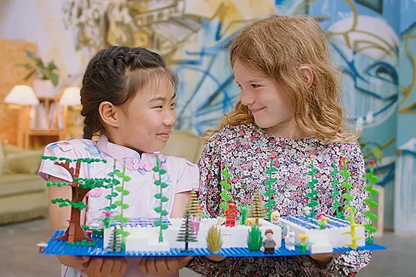 Zwei Kinder lächeln sich an und halten ein farbenfrohes Modell mit Pflanzen. Emotionale Szene für Werbefilm, Filmproduktion oder Imagevideo mit Fokus auf Kreativität, Nachhaltigkeit und spielerisches Lernen.