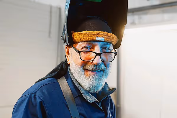 Filmproduktion und Imagefilm-Szene: Porträt eines erfahrenen Mitarbeiters mit Schweißermaske – authentische Recruitingfilm-Visualisierung, die Handwerk, Erfahrung und Menschlichkeit in einem modernen Unternehmenskontext zeigt.