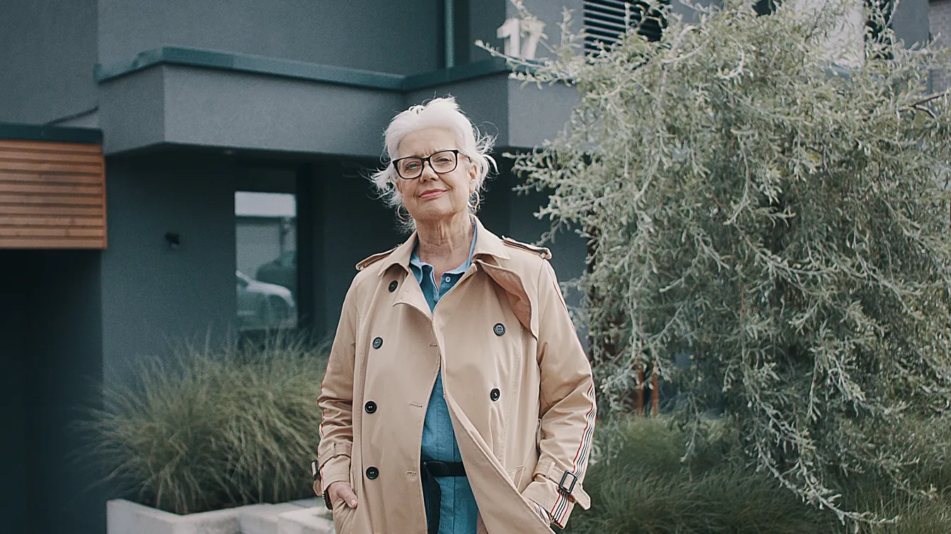 Selbstbewusste ältere Frau steht vor modernem Haus. Authentische Szene für Werbefilm, Filmproduktion oder Imagevideo, die Vertrauen, Lebensfreude und Charakter zeigt – ideal für emotionale Markenkommunikation.