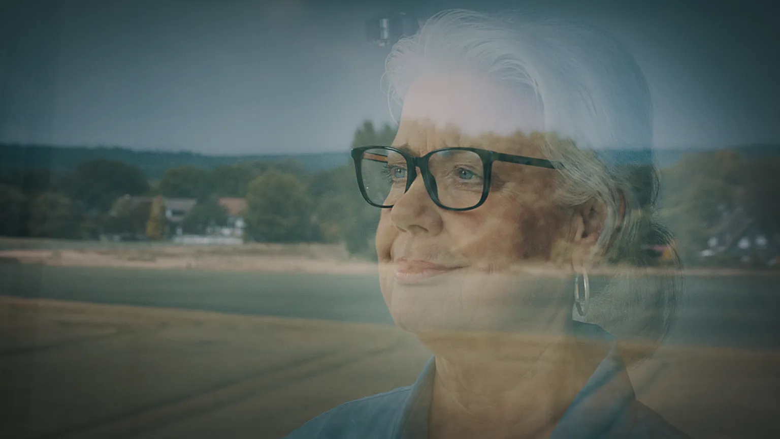 Nachdenkliche Frau blickt durch ein Fenster mit Landschaftsreflexion. Emotionale Szene für Werbefilm, Filmproduktion oder Imagevideo – symbolisiert Ruhe, Erfahrung und Perspektive in authentischer filmischer Inszenierung.