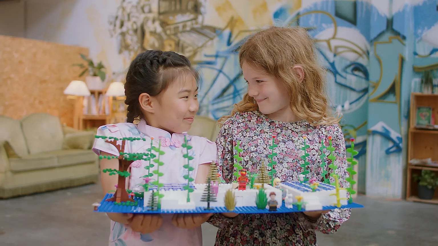 Zwei Kinder halten gemeinsam ein buntes Modell und lächeln sich an. Herzliche Szene für Werbefilm, Filmproduktion oder Imagevideo – zeigt Freundschaft, Kreativität und spielerisches Lernen mit positiver Markenbotschaft.