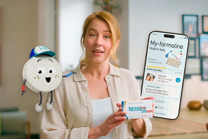 Szene aus einem Werbefilm: Frau präsentiert Formoline L112 mit Smartphone-App und animiertem Maskottchen – moderne Markenkommunikation über Gesundheit und Ernährung.