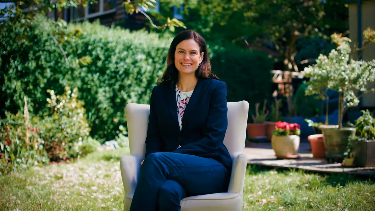 Frau sitzt lächelnd auf einem Stuhl im Garten – Szene aus einem Imagefilm, die Natürlichkeit, Vertrauen und moderne Unternehmensdarstellung in filmischer Ästhetik vermittelt.