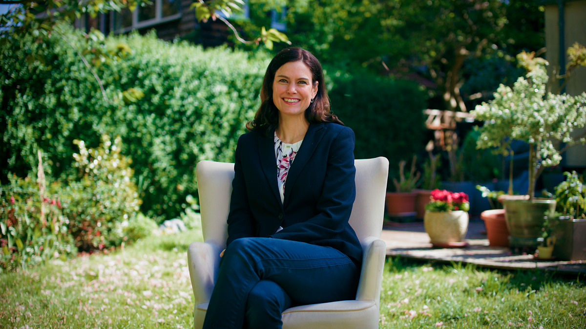 Frau sitzt lächelnd auf einem Stuhl im Garten – Szene aus einem Imagefilm, die Natürlichkeit, Vertrauen und moderne Unternehmensdarstellung in filmischer Ästhetik vermittelt.
