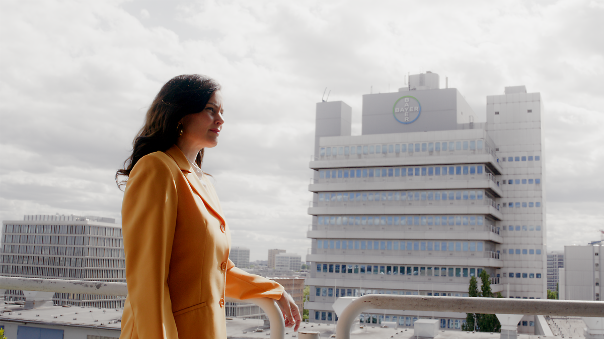 Frau in gelbem Blazer blickt über die Skyline einer Stadt – moderne Szene aus einem Imagefilm, die Professionalität, Zukunftsorientierung und Unternehmensidentität filmisch hervorhebt.