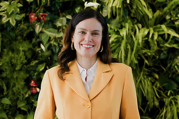 Frau in gelbem Blazer lächelt vor grüner Pflanzenwand – professionelle Szene aus einem Imagefilm, die Authentizität, Nachhaltigkeit und Unternehmenswerte filmisch vermittelt.