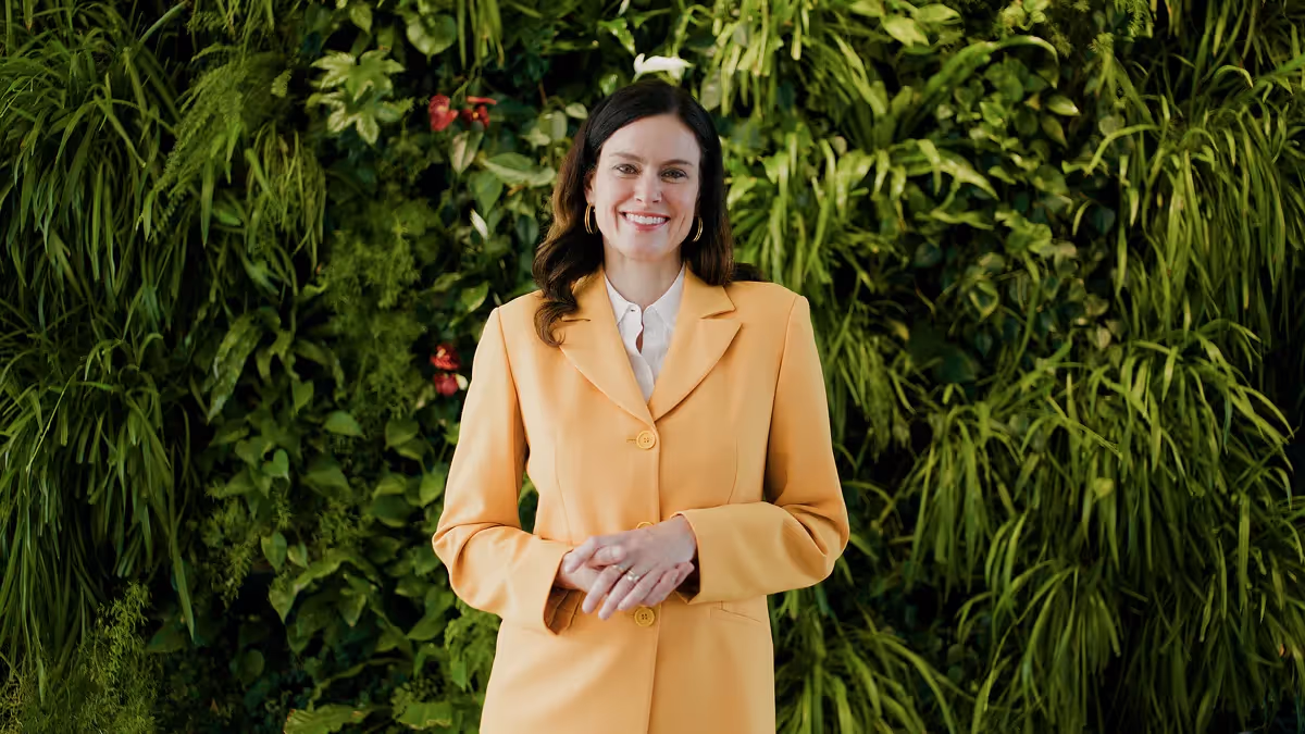 Frau in gelbem Blazer steht vor grüner Pflanzenwand – Szene aus einem Imagefilm, die Nachhaltigkeit und moderne Unternehmenskommunikation in filmischer Bildsprache darstellt.