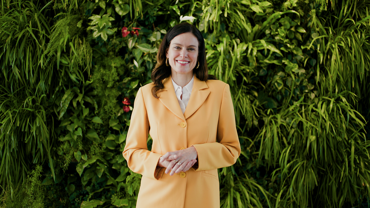 Frau in gelbem Blazer steht vor grüner Pflanzenwand – Szene aus einem Imagefilm, die Nachhaltigkeit und moderne Unternehmenskommunikation in filmischer Bildsprache darstellt.