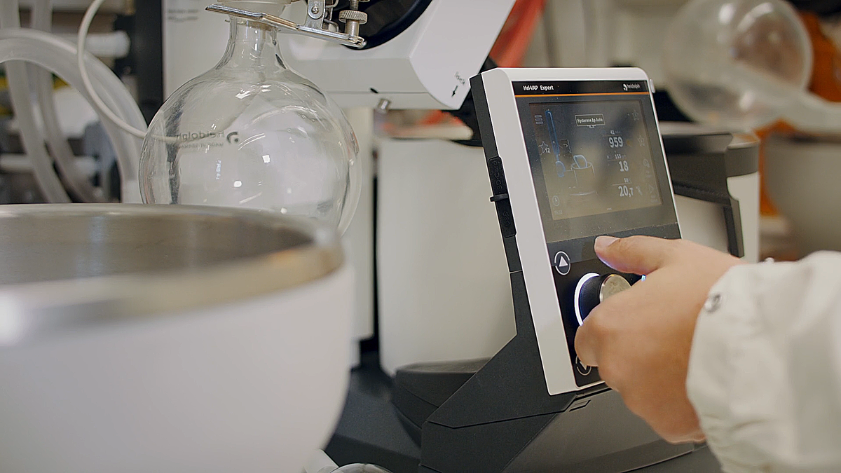 Szene aus einem Imagefilm im Labor: Eine Person bedient ein digitales Steuergerät zwischen Laborgeräten – moderne Filmproduktion mit Fokus auf Technologie, Forschung und Präzision.