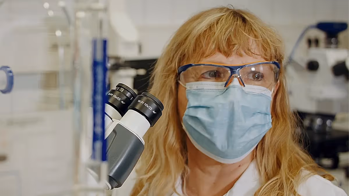 Imagefilm-Szene: Forscherin im Labor mit Schutzbrille und Maske neben Mikroskop – professionelle Filmproduktion, die Forschung, Innovation und wissenschaftliche Präzision visuell hervorhebt.