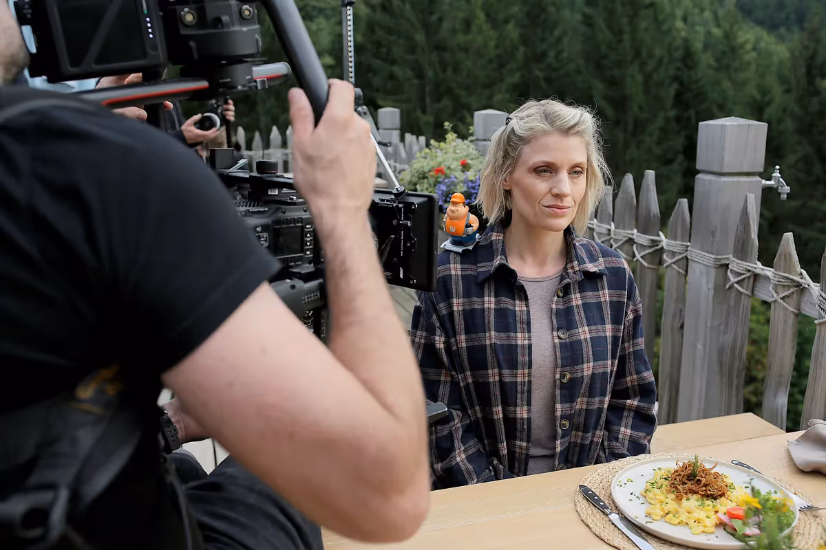 Filmszene aus einer professionellen Filmproduktion: Kameramann filmt eine Schauspielerin am gedeckten Tisch im Außenbereich. Authentische Drehsituation mit Kamera-Setup, Licht und Crew – Realfilm-Produktion für Imagefilm und Markenkommunikation.