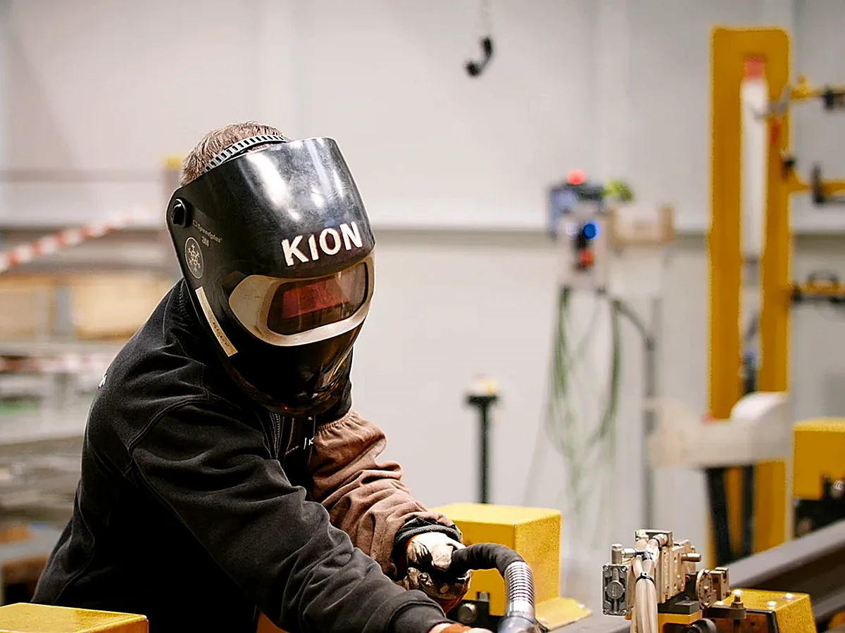Schweißer mit KION-Schweißhelm an einer Werkbank, Szene aus dem Kundenfilm für KION