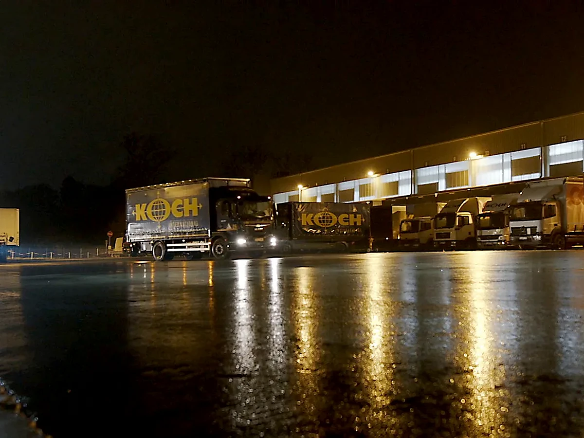 Nächtlicher Logistikhof mit Koch-Lkw und Spiegelungen auf nassem Asphalt, Kundenfilm für proLogistik