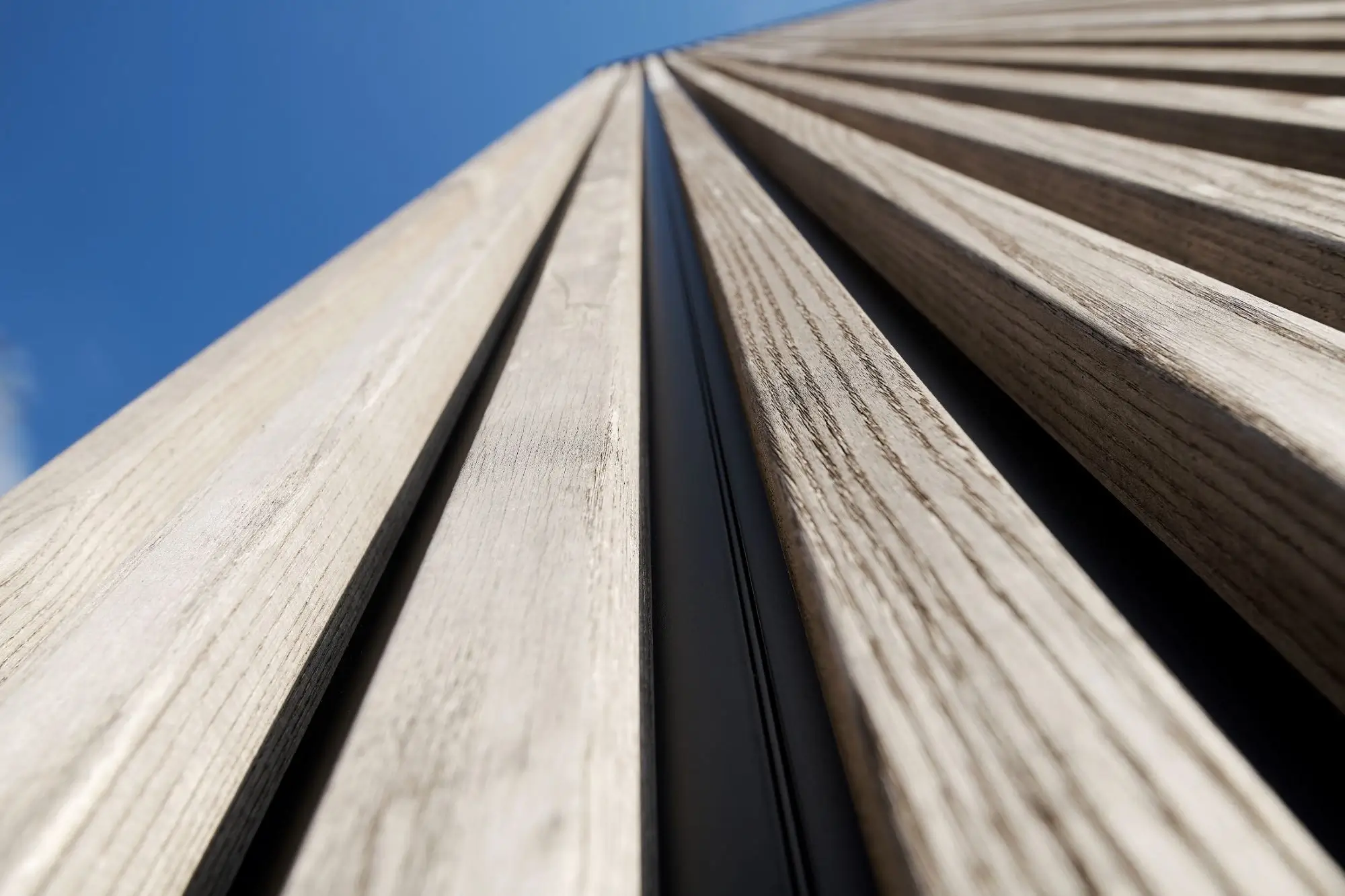 Nahaufnahme von vertikalen Holzlatten an einer Fassade vor blauem Himmel.