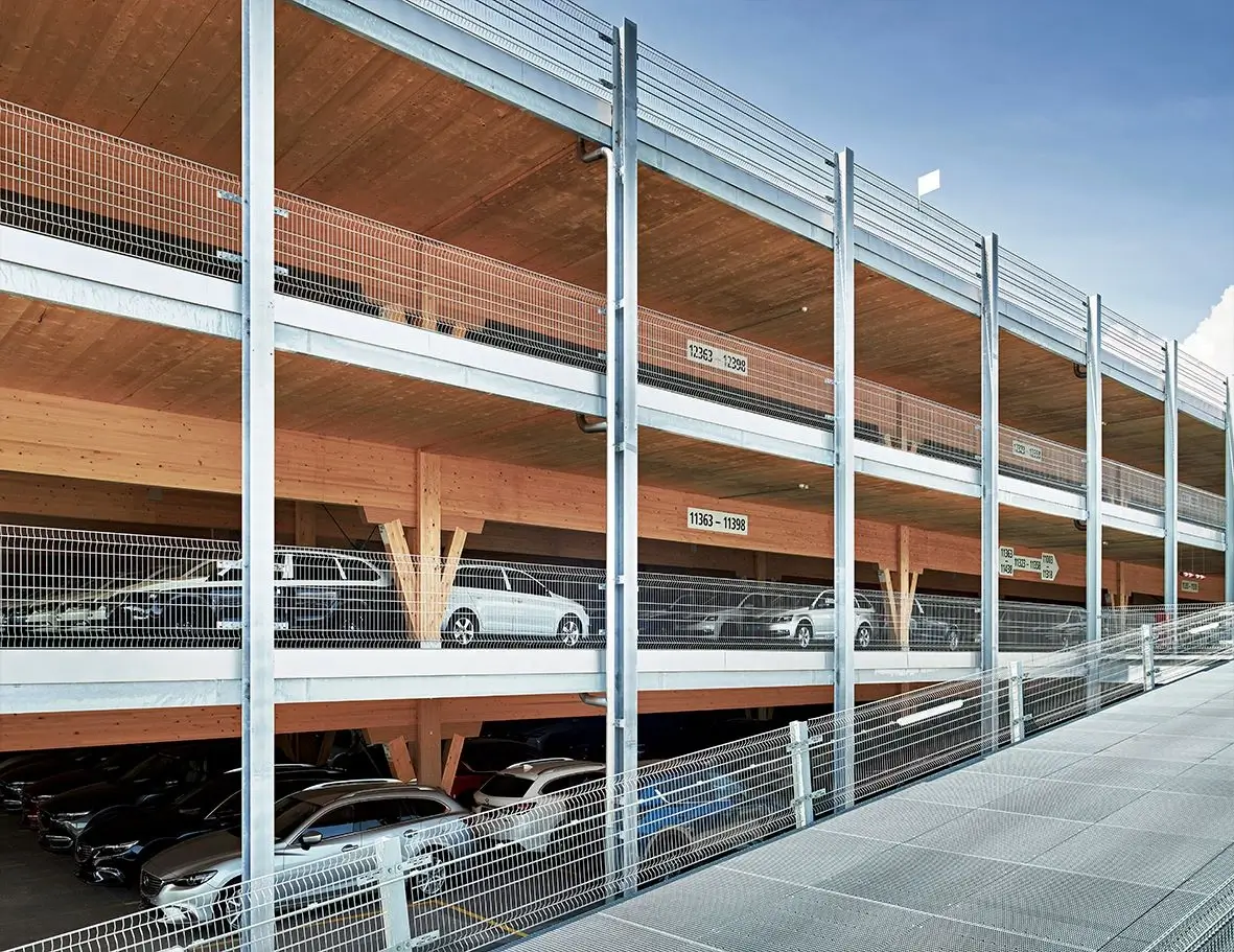 Mehrstöckige Parkgarage mit Holzbalken und Metallgeländer, mehrere geparkte Autos sichtbar.