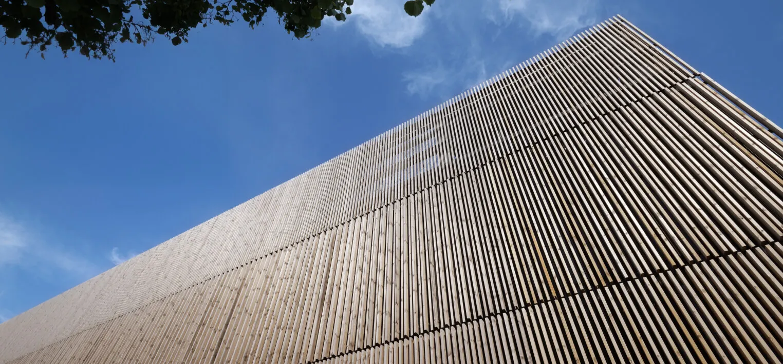 Moderne Fassade aus vertikalen Holzlatten unter blauem Himmel mit wenigen Wolken.