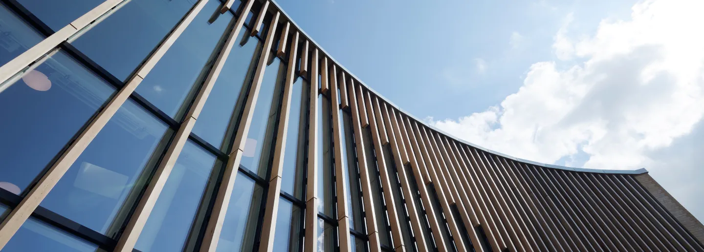 Moderner Gebäudefassade mit großen Glasfenstern und vertikalen Holzlamellen unter blauem Himmel.