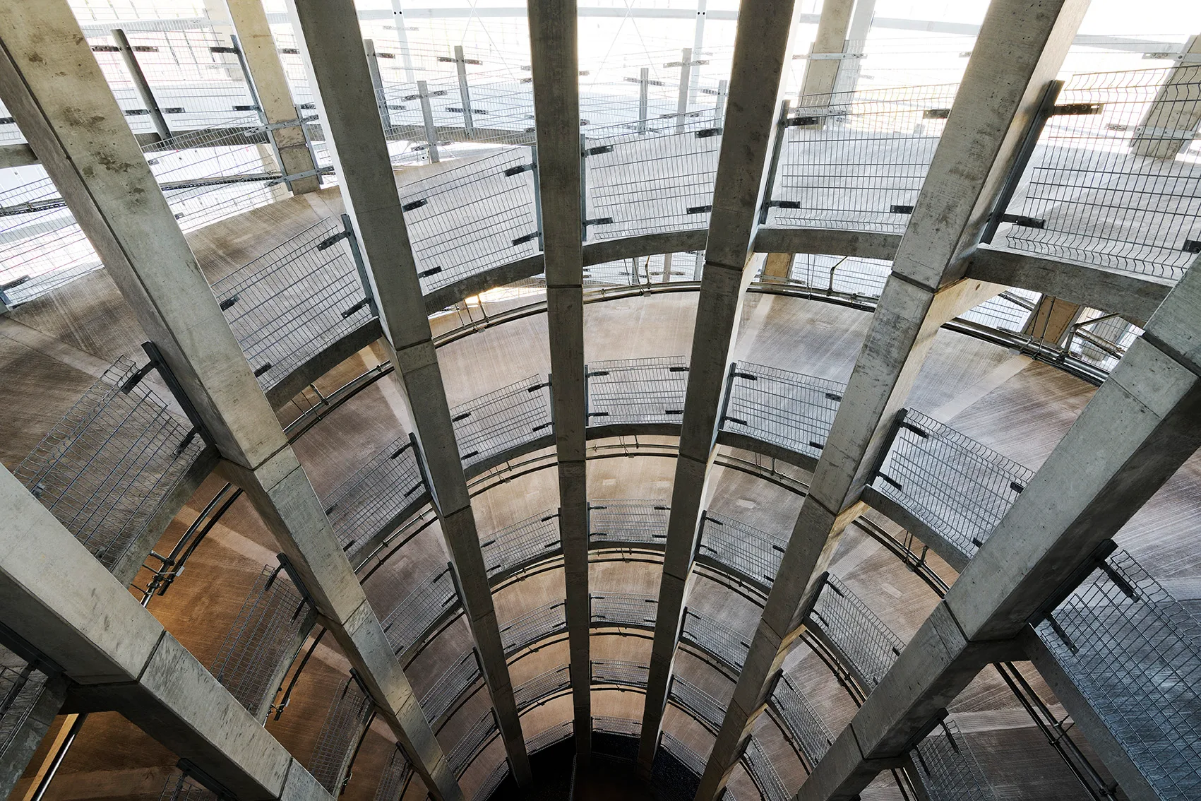 Innenansicht einer spiralförmigen Tiefgarage mit sichtbaren Betonsäulen und Metallgeländern.