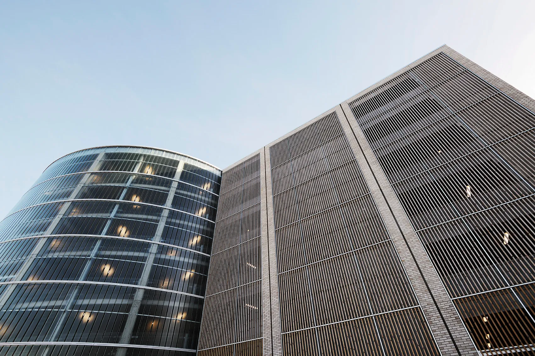 Blick nach oben auf moderne Gebäude mit Glas- und Metallfassaden vor klarem Himmel.