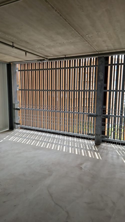 Leerer, lichtdurchfluteter Innenraum mit einem Gitterfenster, das Sonnenstreifen auf den Betonboden wirft.