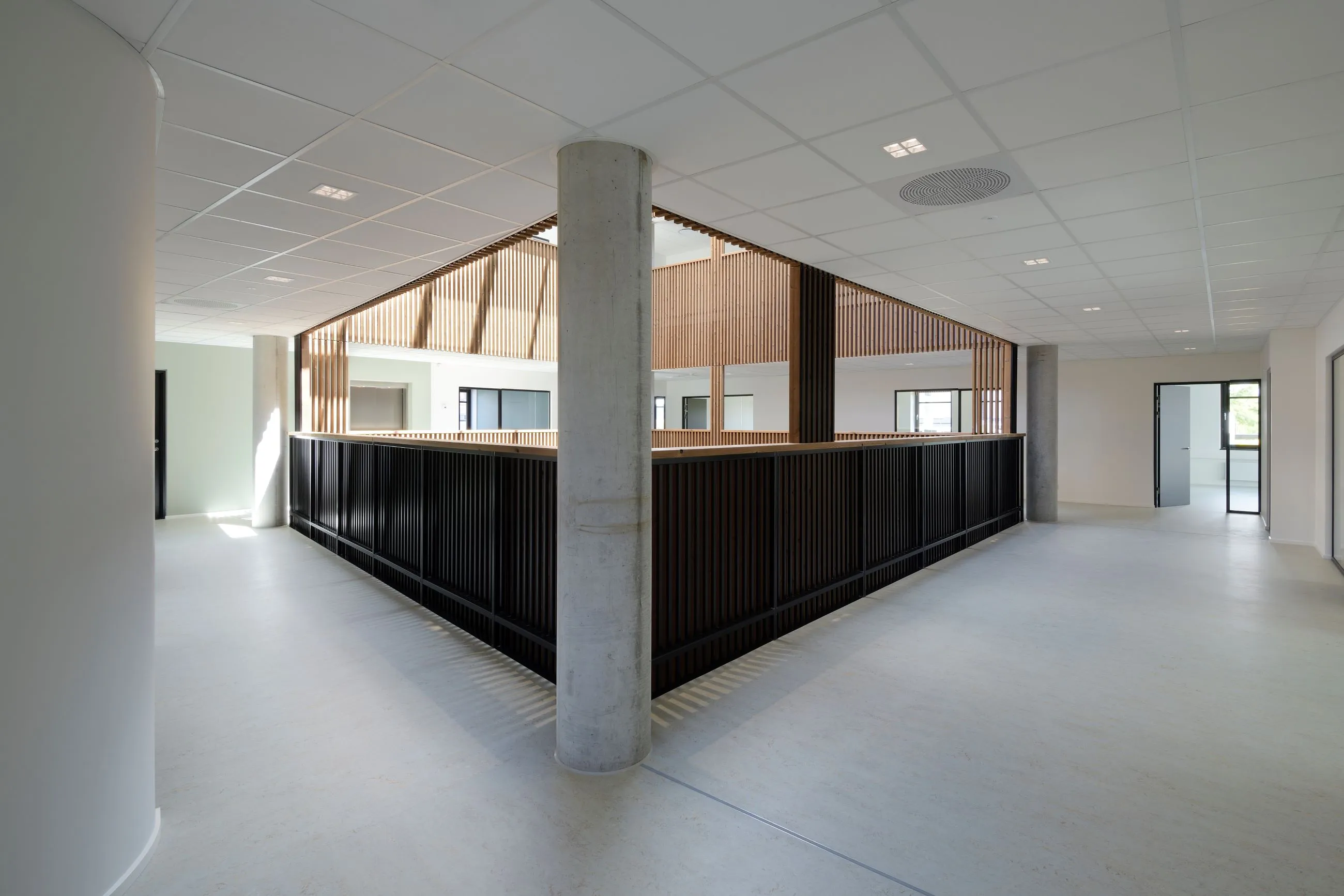 Woodfac Click, Aluminium-Struktur: Innenraum mit Betonstütze und Brüstung aus dunklen Lamellen, Holzlamellen darüber