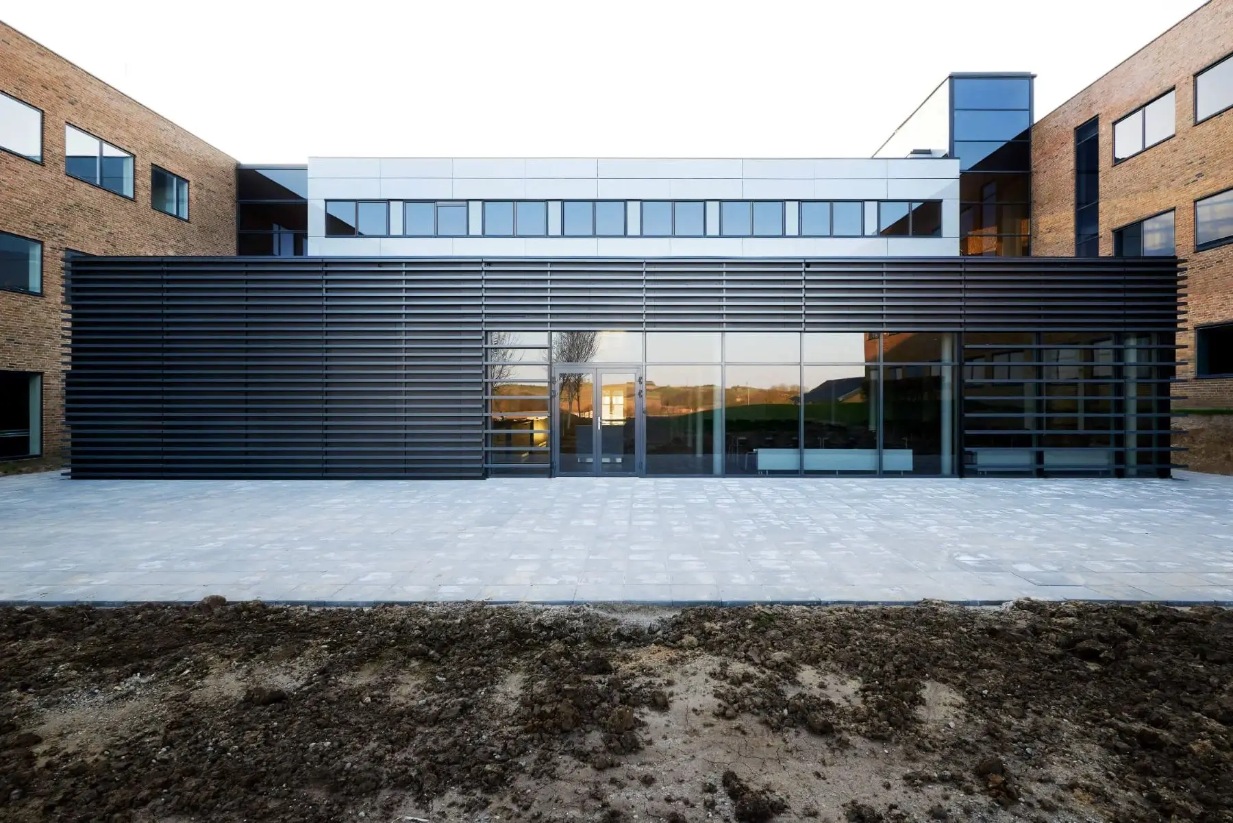 Bürogebäude mit dunkler horizontaler Lamellenfassade vor Glasfront und Backsteinflügeln