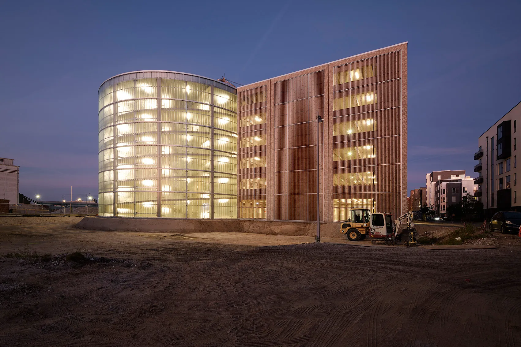 Parkhaus Søndre Havn in Køge in der Abenddämmerung mit Holzfassade und beleuchtetem Rundturm, Woodfac Click & Napsu