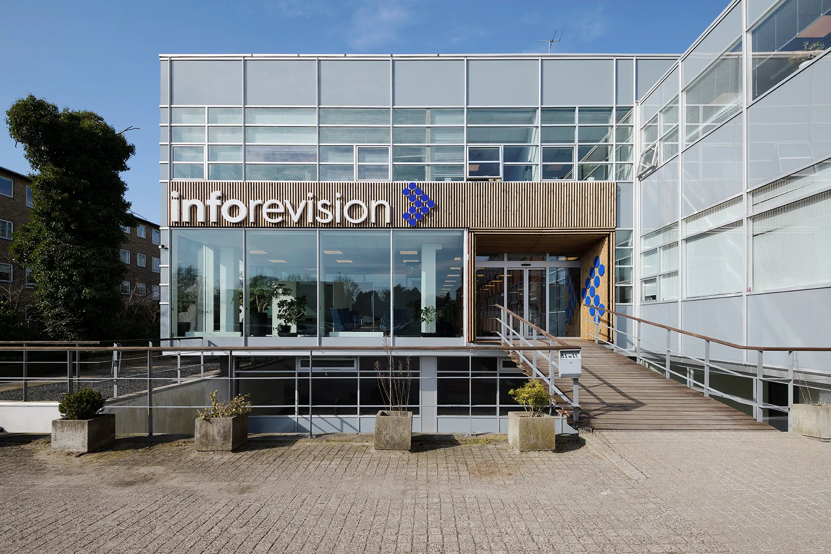 Gebäude von Inforevision mit Woodfac Panel Holzlamellen am Eingang und Firmenschriftzug vor Glasfassade