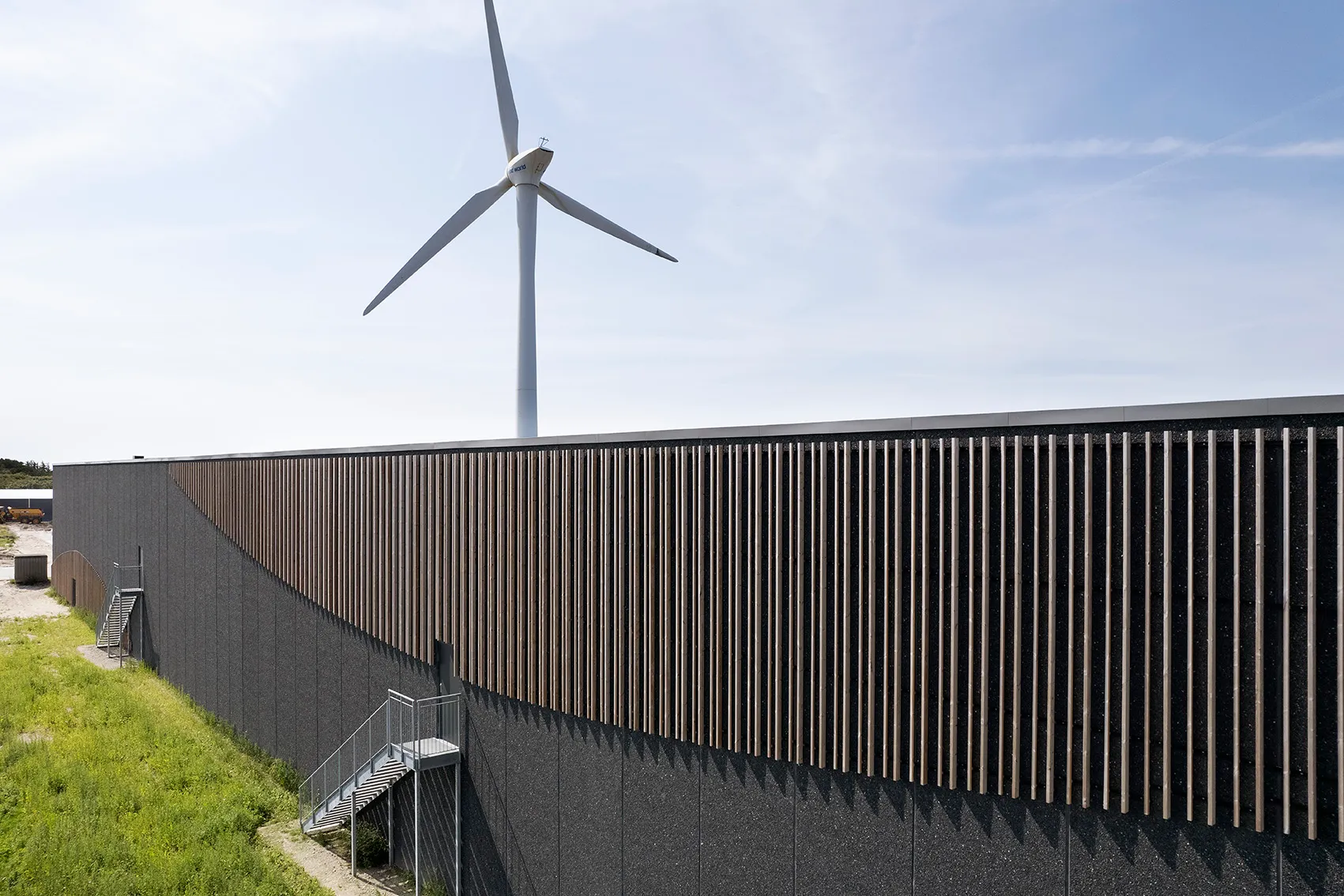 Skagen Salmon: Fabrikhalle mit dunkler Fassade und Holzlamellen, Windrad im Hintergrund, Woodfac Click