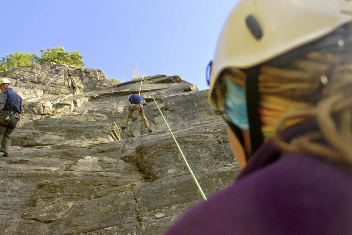 An over the shoulder view of a woman belaying a climbing on a top-rope route. 