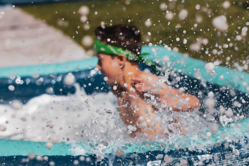 A young boy splashing into a kiddy pool at the end of a tarp runway.