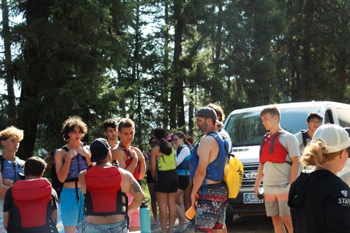A youth group standing by camp vans in their rafting gear, waiting for rafts to be unloaded.