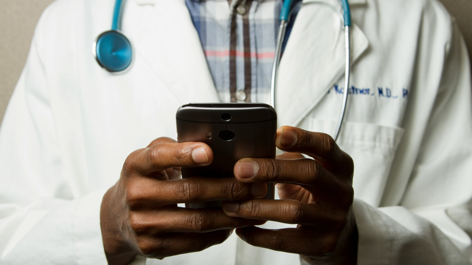 Doctor wearing a lab coat holding a smartphone, checking information.