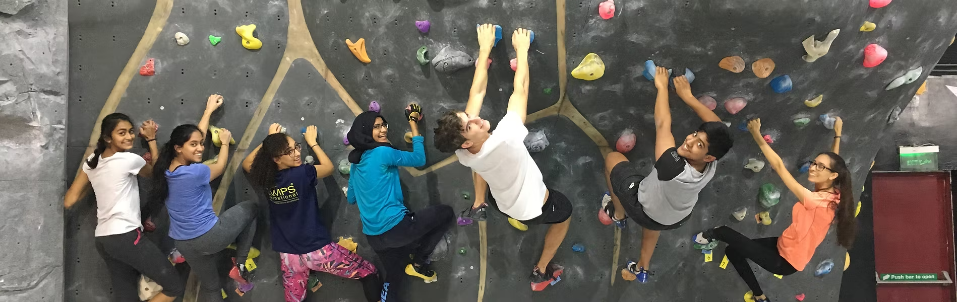 Friends climbing colorful indoor bouldering walls together at a gym in Dubai