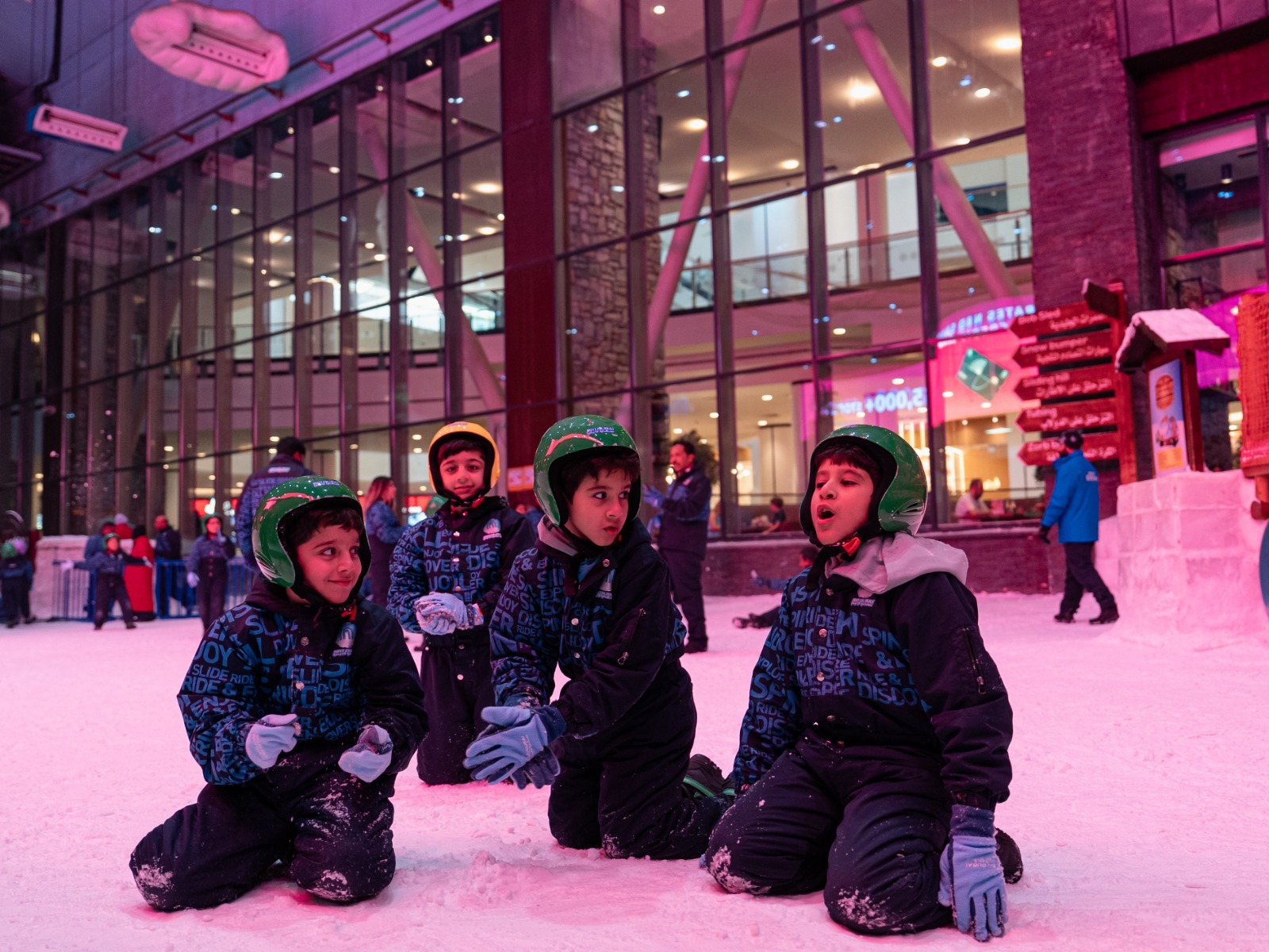 Children playing in the snow at Ski Dubai indoor winter park, wearing helmets and snow gear for a festive holiday adventure.