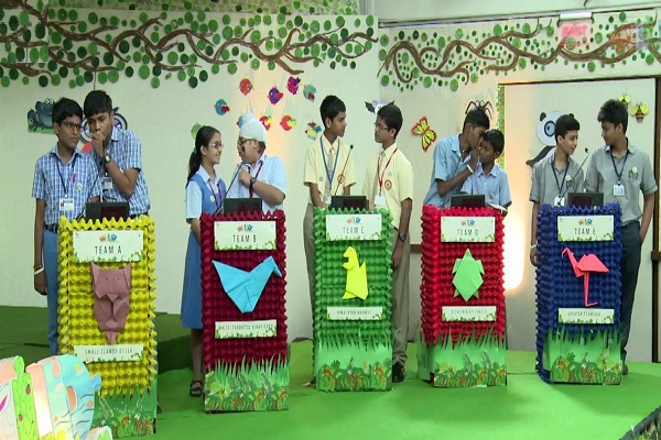 School students participating in a lively interschool quiz competition, standing in teams behind colorful podiums decorated with origami animals – a fun and educational group activity that promotes teamwork and general knowledge.