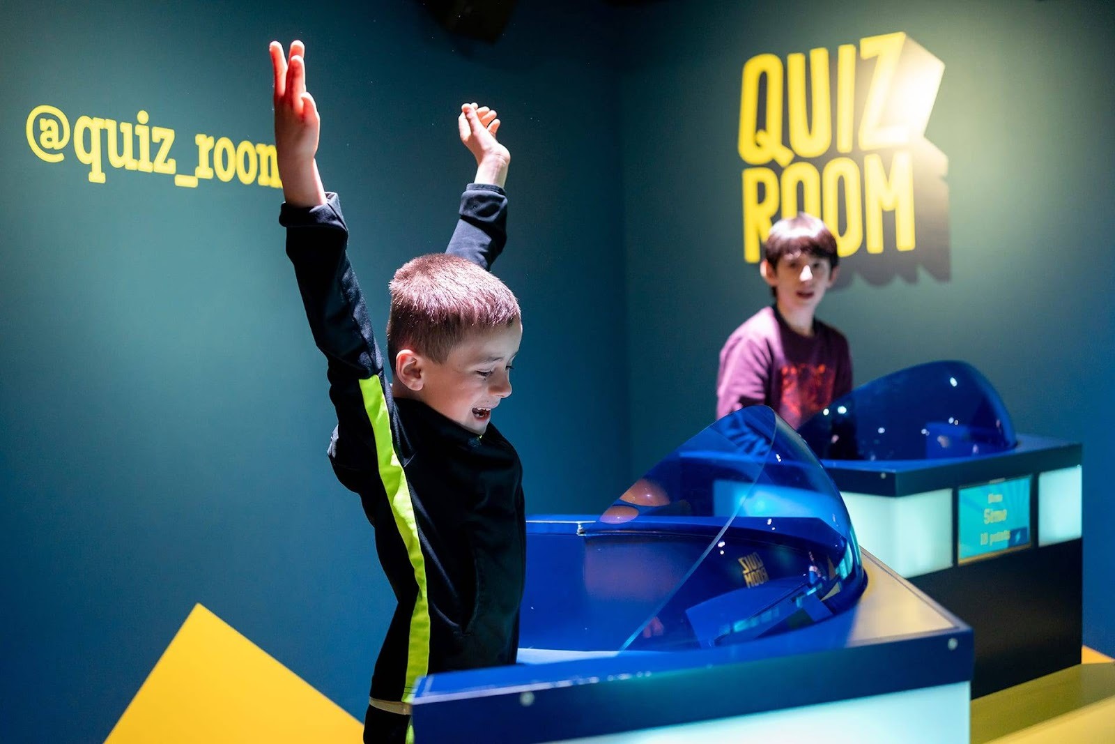 A child celebrates a correct answer at Quiz Room Dubai, hands raised in victory during an immersive quiz game show experience designed for kids.