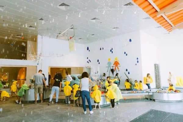 Kids in raincoats exploring water play zone at OliOli Dubai — interactive indoor museum for children.