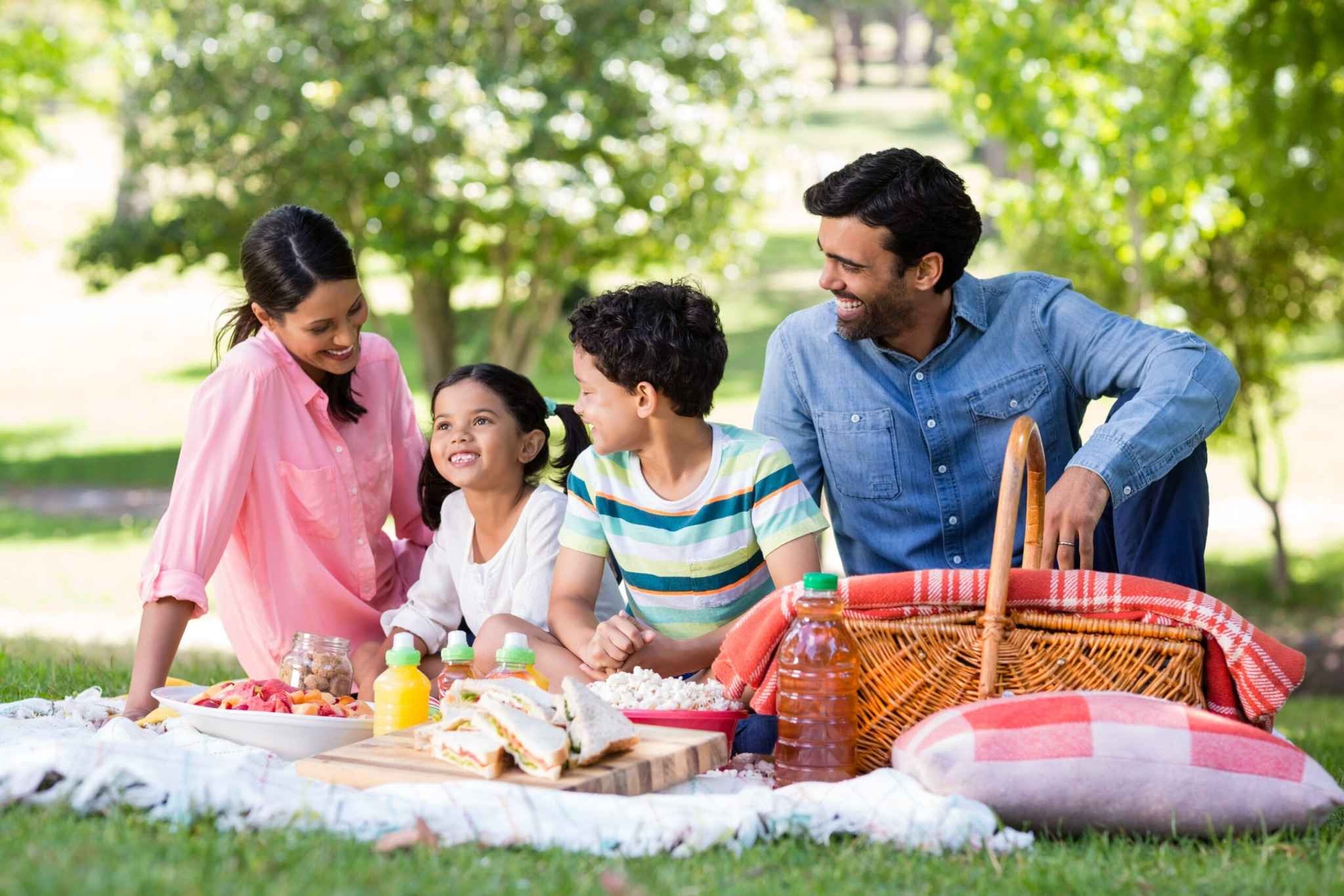Family enjoying a sunny picnic in a green park in Dubai, surrounded by trees and healthy snacks — ideal for a peaceful day out at Al Barari Nature Escapes.