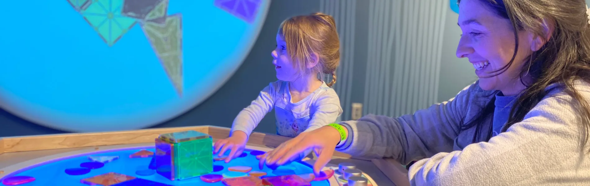 Mother and child exploring a hands-on science exhibit at OliOli Children’s Museum in Dubai, with interactive lights and playful learning.