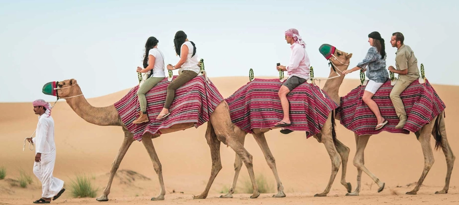 Tourists riding camels through Dubai desert on a guided safari tour — family-friendly cultural adventure with traditional Bedouin experience