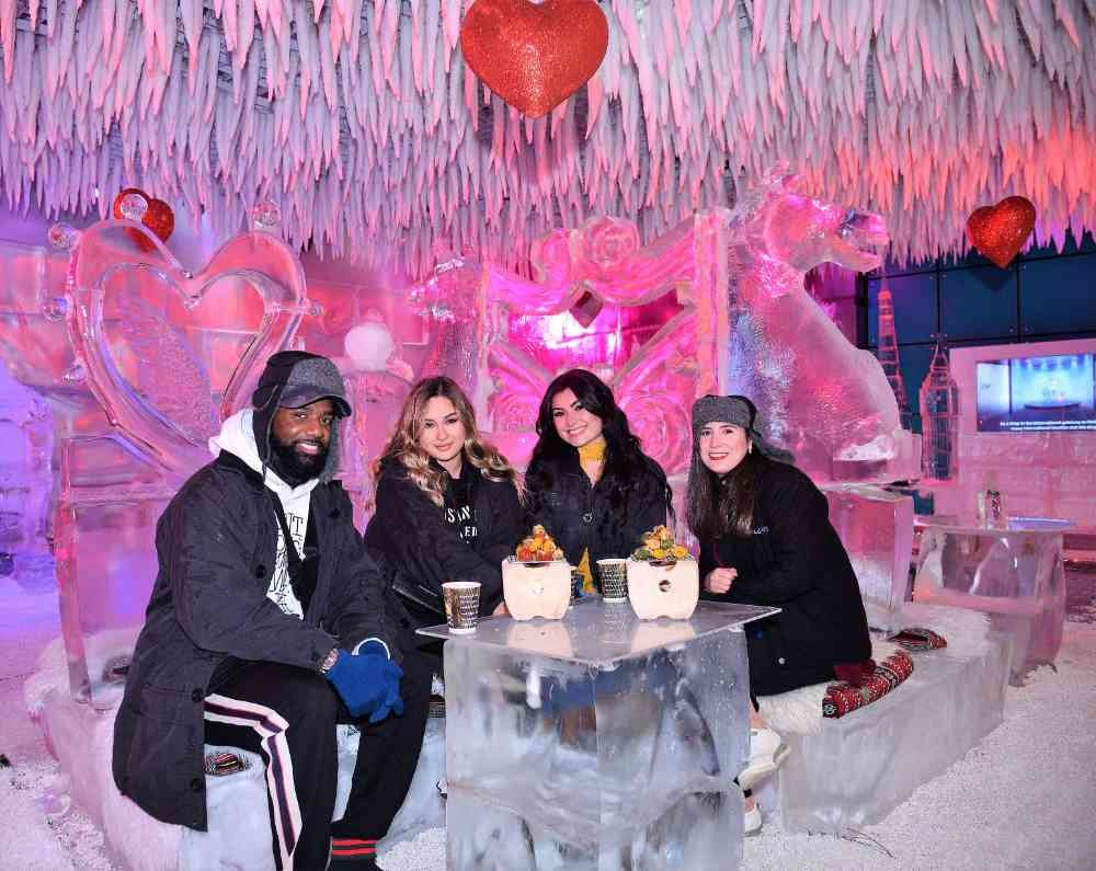 Friends enjoying drinks and snacks at an ice bar in Dubai surrounded by colorful ice sculptures