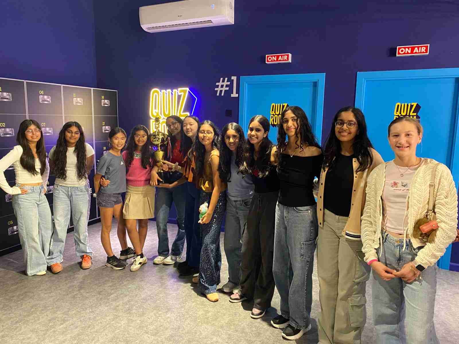  Large group of teenage girls posing with a trophy after a birthday quiz game at Quiz Room Dubai