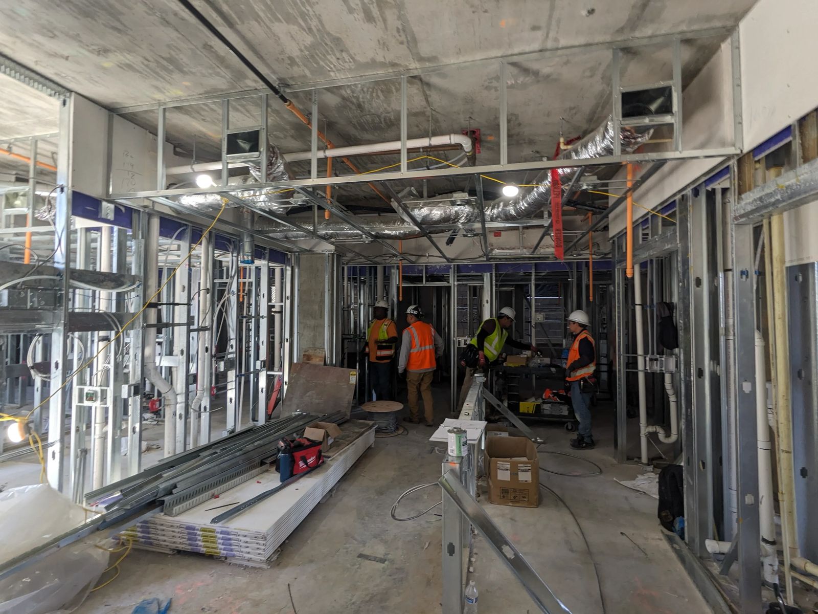 Crew in hard hats and safety vests working among metal stud wall and ceiling framing inside a building under construction