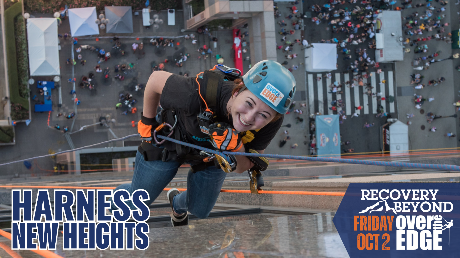 Smiling woman in helmet and harness rappelling down a tall building over a city street. Harness New heights is Recovery Beyond's fundraiser. Recovery Beyond partnered with Over The Edge to offer a unique adventure for members and donors to support the work of this non-profit: providing events and activities that build community and shared experiences that help make long term sobriety sustainable.