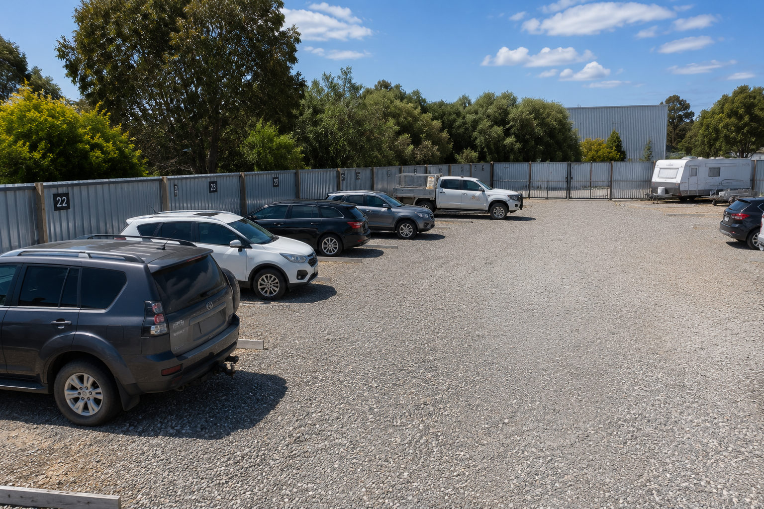 Cars and 4WDs parked in numbered bays in a fenced gravel car park.