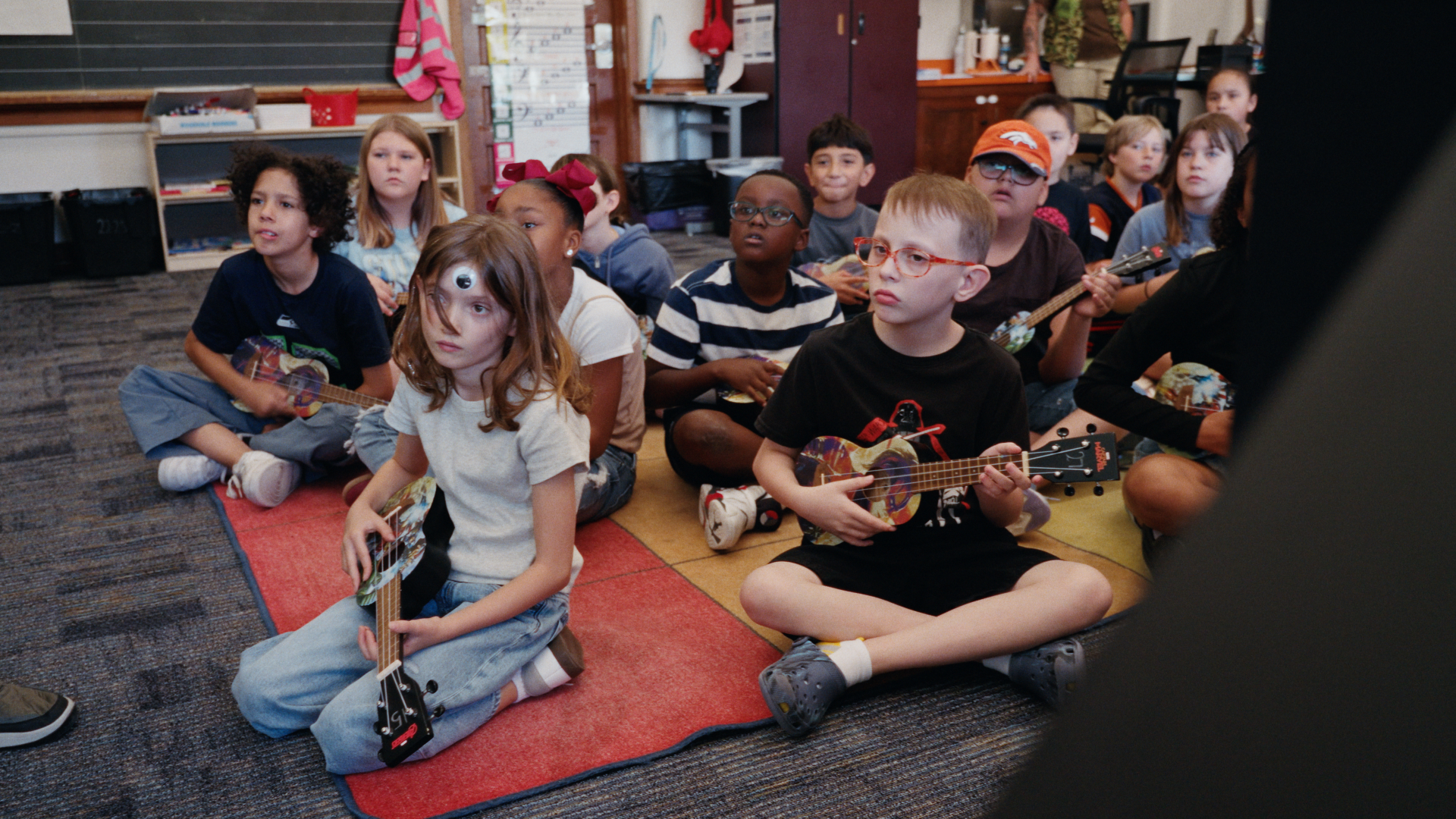 Students playing ukuleles on a classroom rug
