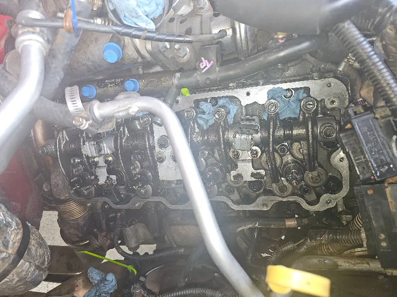 Heavy-duty engine repair service showing exposed rocker arms and valve train during cylinder head work, blue shop towels packed in ports.